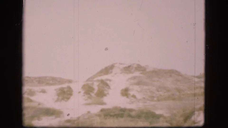 1975 Denmark home-movie frame of a dune ridge with muted grasses and soft 8mm exposure.