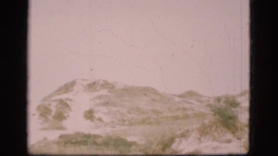 1975 Denmark 8mm still showing a low sandy slope with scrub grasses in hazy light.