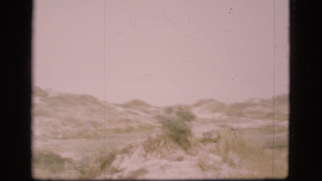 1975 Danish 8mm frame showing grassy sand dunes and a pale overcast sky during a coastal landscape pan.