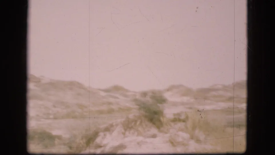 1975 Danish 8mm frame showing grassy sand dunes and a pale overcast sky during a coastal landscape pan.