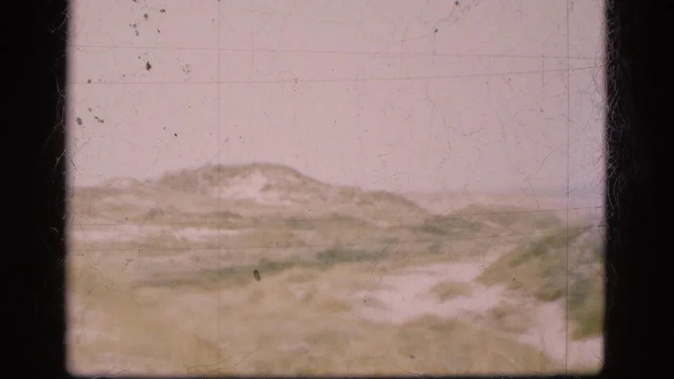 1975 Danish coastal dune ridge with sparse grass, soft focus, and visible 8mm film texture.