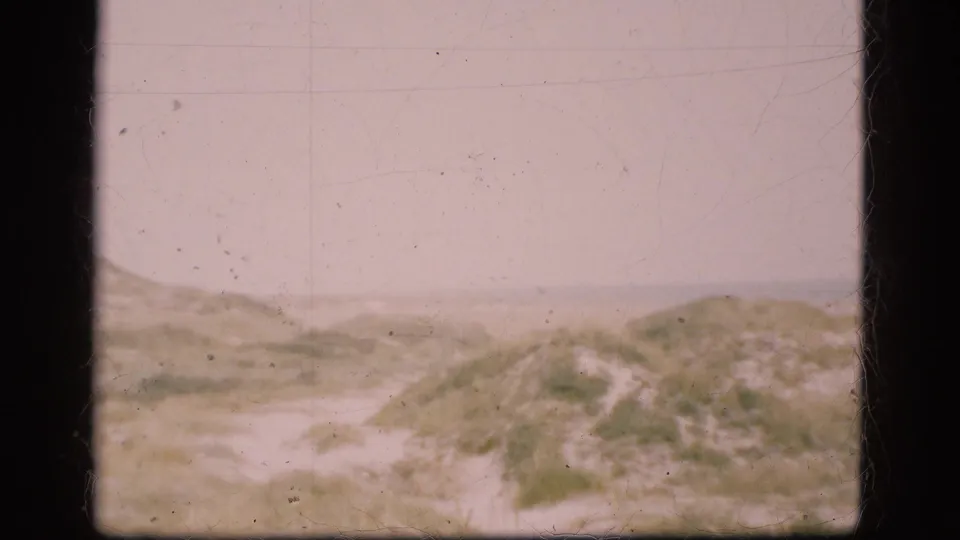 1975 Danish coastal landscape frame with a sandy path, grassy dunes, and pale horizon in soft 8mm color.