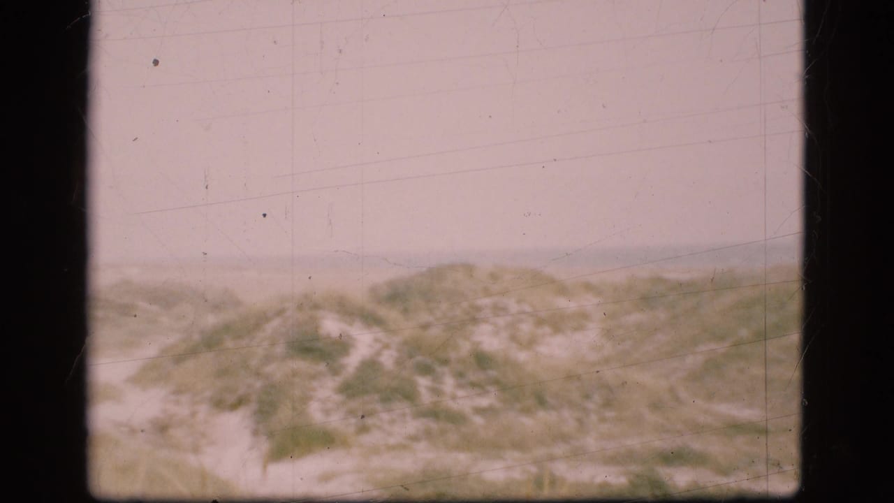 Low coastal dunes and sand path seen through faded 8mm film.