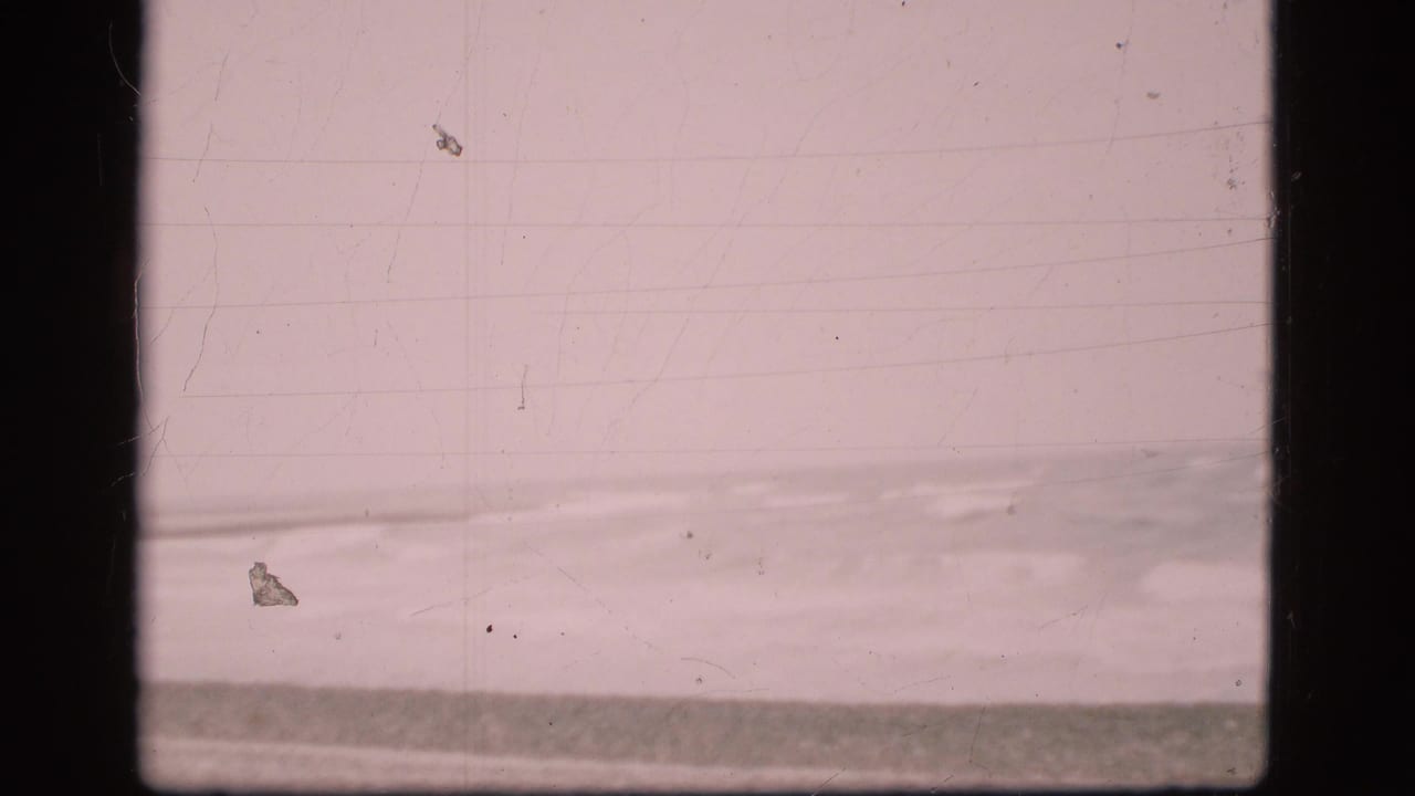 Vintage 8mm view of the Danish shoreline, with a grey sea band, pale sky, and soft surf near the beach.