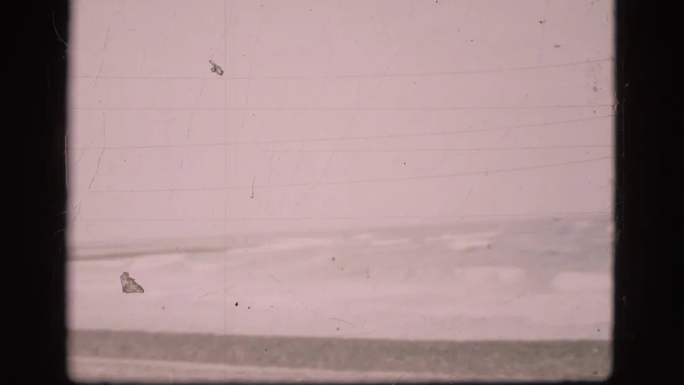 Vintage 8mm view of the Danish shoreline, with a grey sea band, pale sky, and soft surf near the beach.