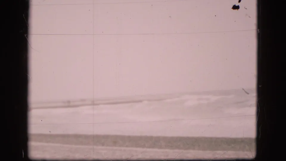End frame of a Danish coastal 8mm shot, showing a quiet sea horizon, breaking waves, and aged film texture.