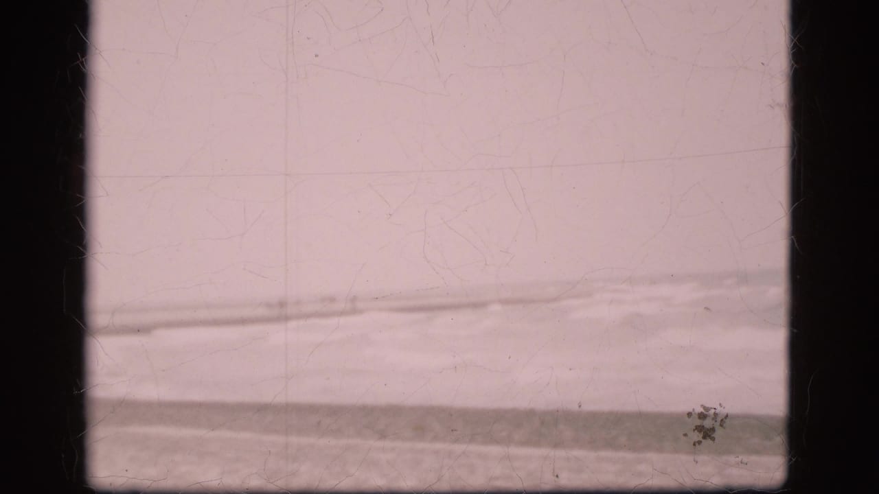 1975 Denmark 8mm frame showing rough water near a low shoreline beneath a pale overcast sky, with visible gate borders and film wear.