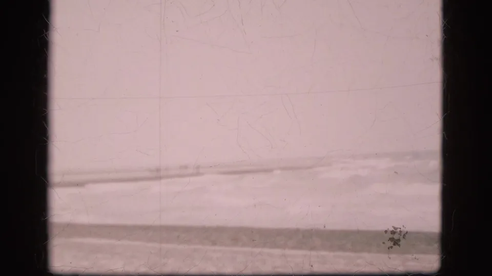 1975 Denmark 8mm frame showing rough water near a low shoreline beneath a pale overcast sky, with visible gate borders and film wear.