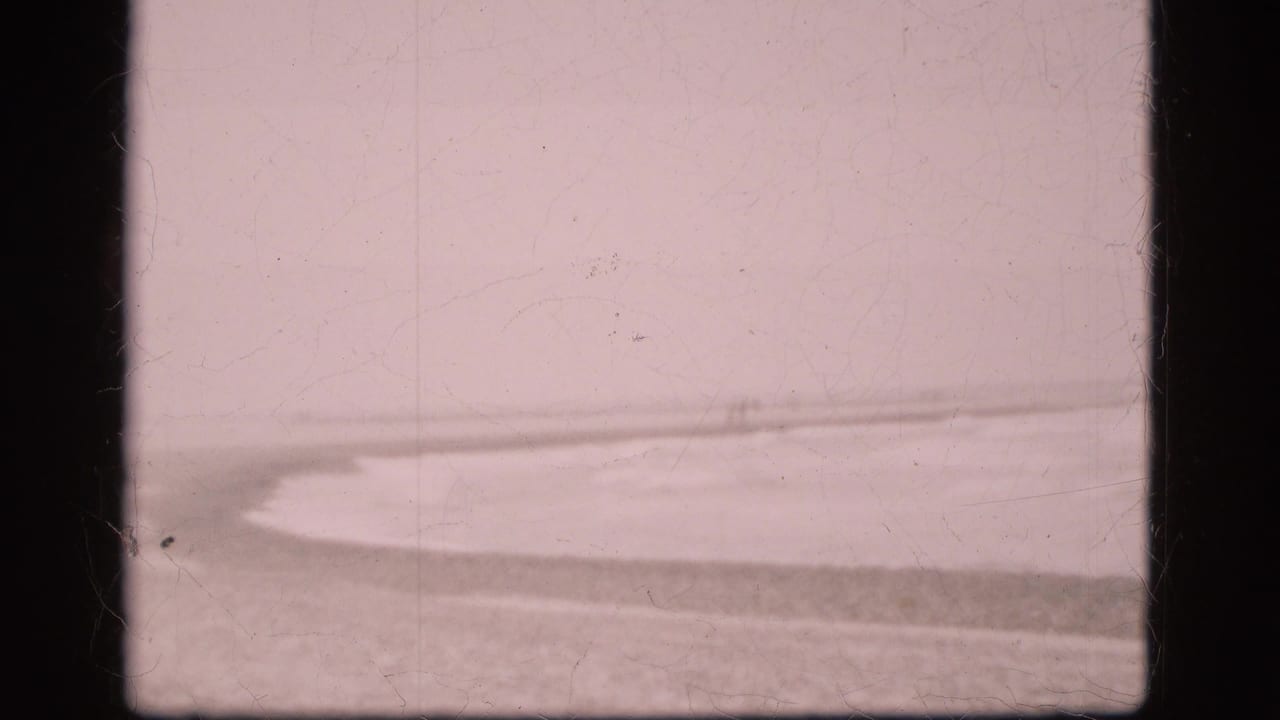 1975 Denmark 8mm view of a low beach horizon and agitated water, with faded pink tone, scratches, and dark frame edges.