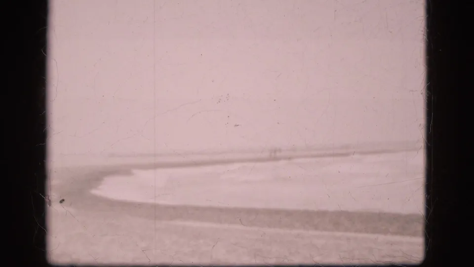 1975 Denmark 8mm view of a low beach horizon and agitated water, with faded pink tone, scratches, and dark frame edges.