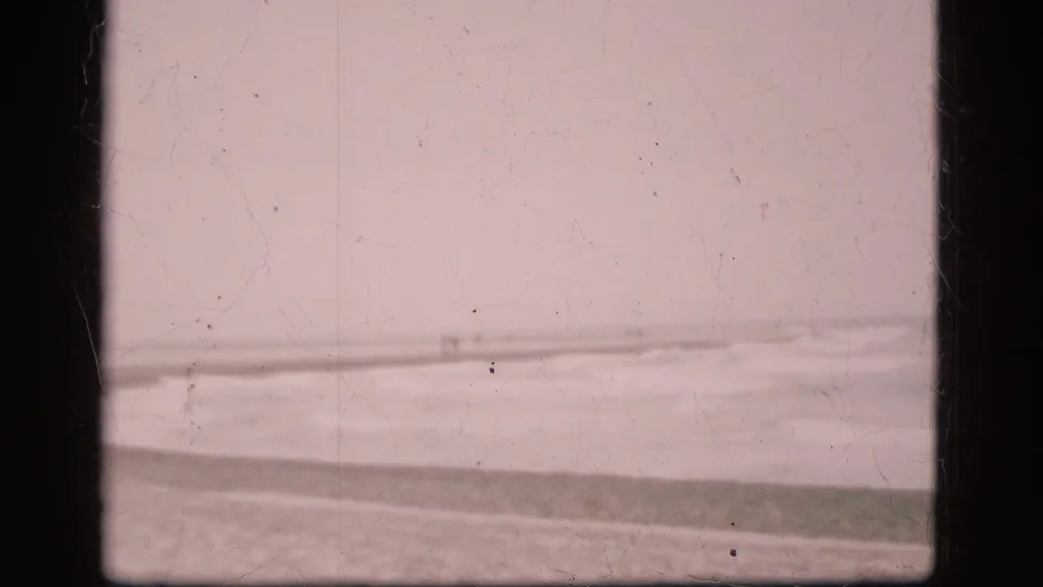 1975 Denmark 8mm view of rough coastal water and a distant shoreline, with soft focus, pink fading, dust, scratches, and dark gate borders.