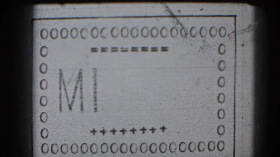 A monochrome 8mm leader frame shows the letters MI forming within a bordered strip, with perforations and guide marks visible.