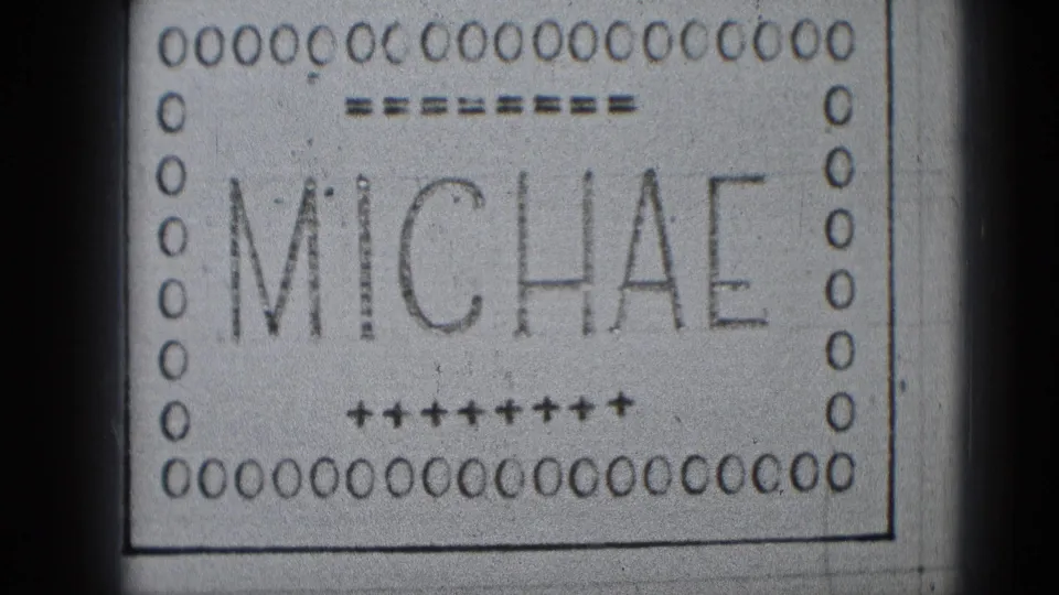A monochrome 8mm leader frame shows MICHAE, nearly completing the name Michael, with perforations and handmade guide marks visible.