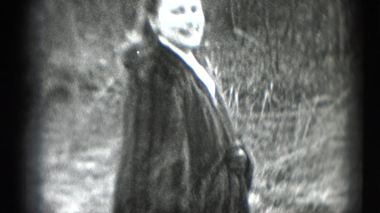 Woman in a dark fur coat smiles outdoors beside low plantings.