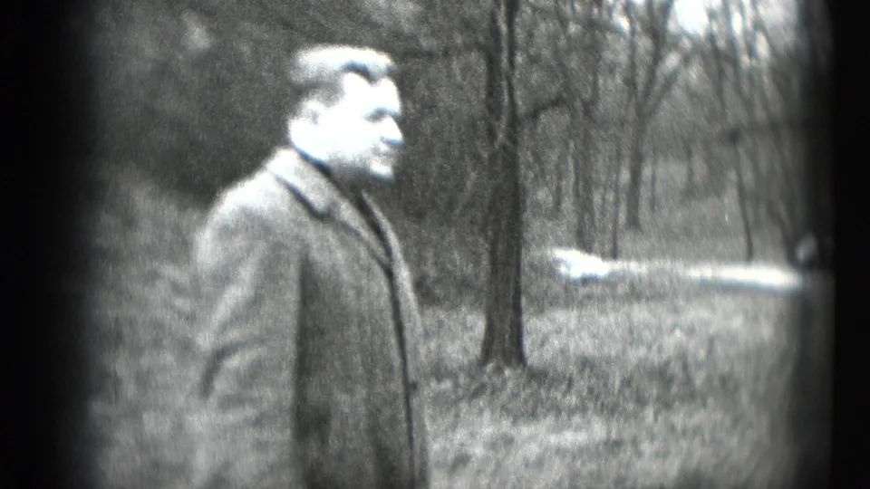 The man turns to the side in a heavy coat, with bare trees and open ground behind him in the 1948 Middletown footage.