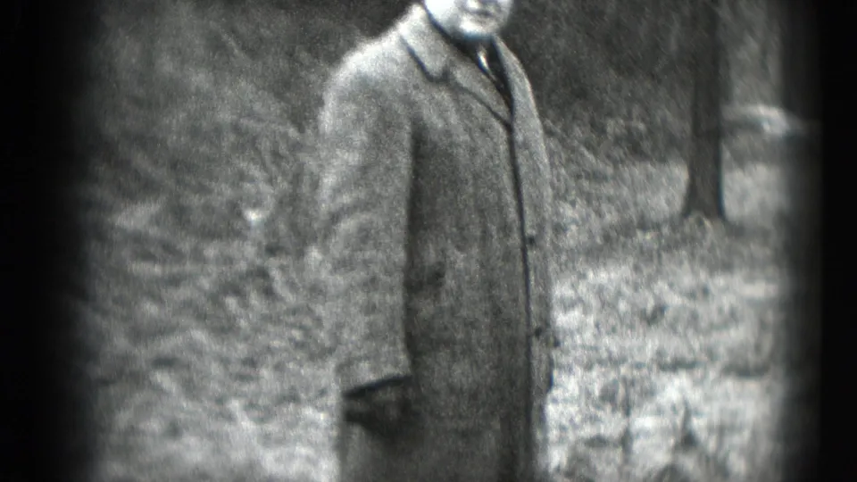 The man continues moving through the wooded outdoor setting, partly cropped by the handheld 8mm frame.