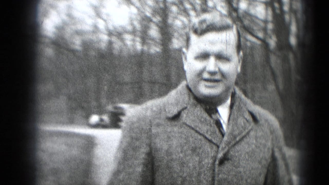 Man in coat faces the camera with a car partly behind him.