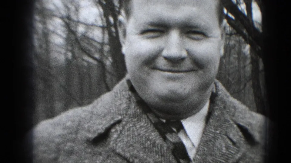 Close-up of the smiling man in a wool coat and tie, filmed outdoors in black-and-white 8mm footage from Middletown.