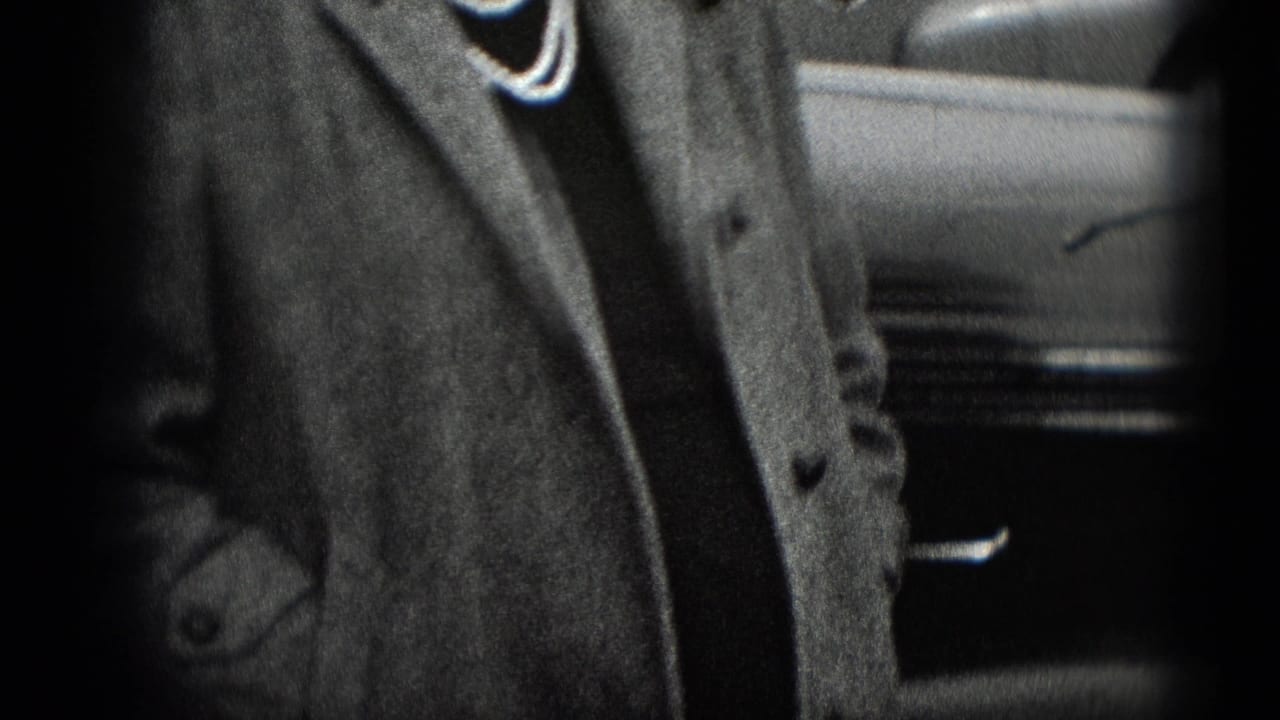 Tight home-movie frame showing a woman's coat and necklace with part of a parked vehicle at the edge.