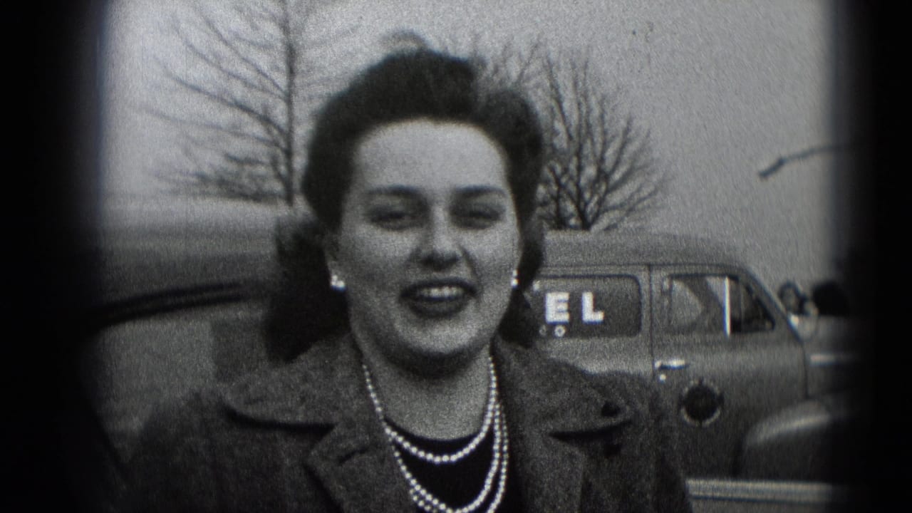 Smiling woman in a coat and pearl necklace faces the camera outdoors in Middletown, Pennsylvania, with a parked car and bare trees behind her.