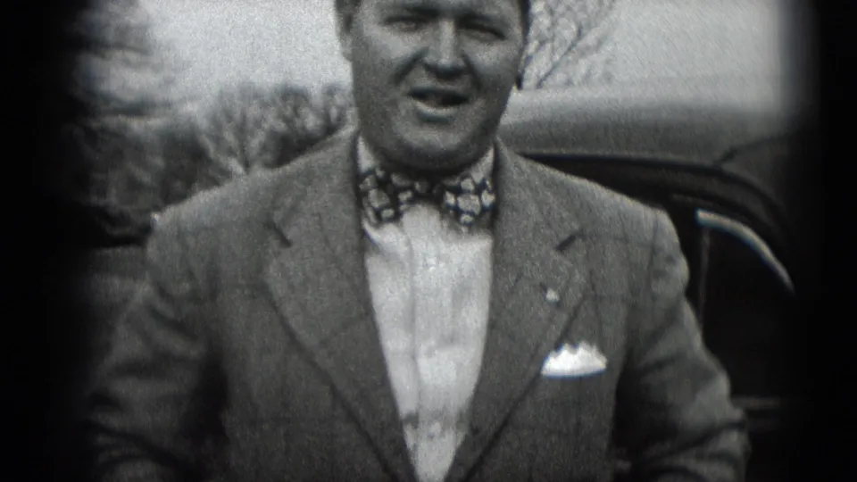 Black-and-white 8mm frame of a well-dressed adult man outdoors in Middletown, Pennsylvania, looking toward the camera near a dark automobile.