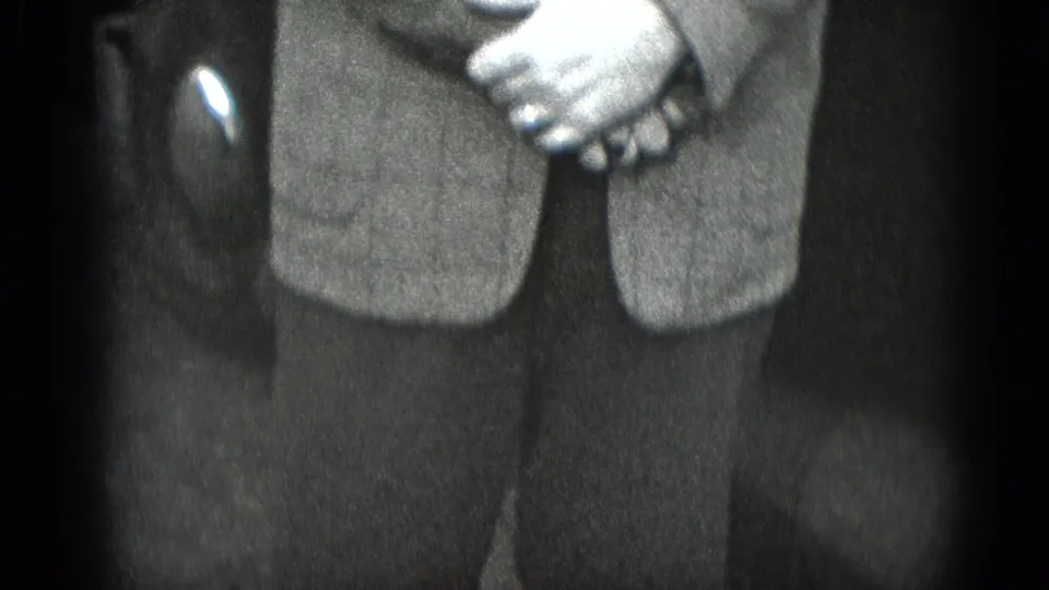 Black-and-white 8mm frame from Middletown, Pennsylvania showing a man's clasped hands over a suit jacket near a car interior.