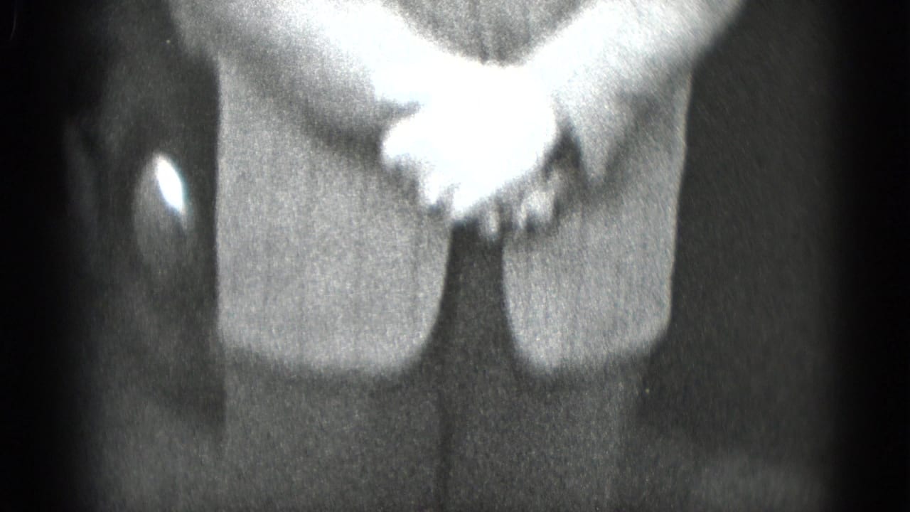 Black-and-white 8mm close-up of clasped hands on a suit jacket, consistent with the clip's late-1940s home-movie setting.