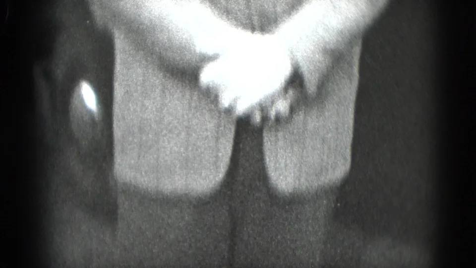 Black-and-white 8mm close-up of clasped hands on a suit jacket, consistent with the clip's late-1940s home-movie setting.