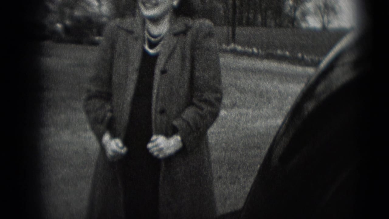 A woman in a long coat and pearl necklace stands outdoors beside a car in 1948 Middletown home-movie footage.