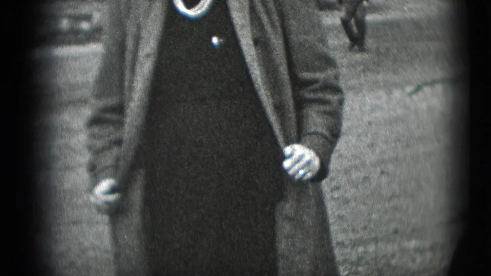 A close 8mm frame shows the woman holding her coat open, with pearls and a dark dress visible in Middletown, Pennsylvania.