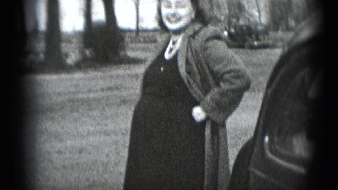 A smiling pregnant woman in a dark dress and coat stands outdoors near a car in Middletown, Pennsylvania home-movie footage.