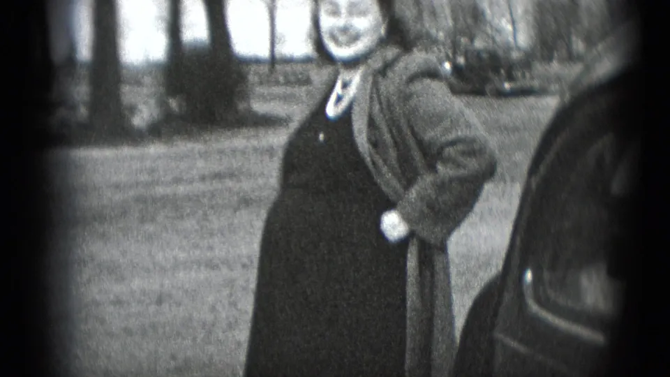 A smiling pregnant woman in a dark dress and coat stands outdoors near a car in Middletown, Pennsylvania home-movie footage.