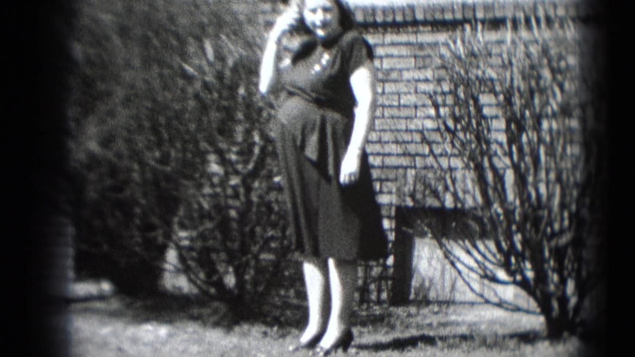 A pregnant woman in a dark dress smiles toward the camera with a telephone receiver near her ear in a Middletown yard.