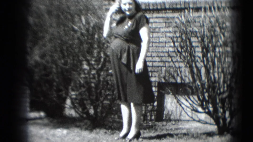 A pregnant woman in a dark dress smiles toward the camera with a telephone receiver near her ear in a Middletown yard.