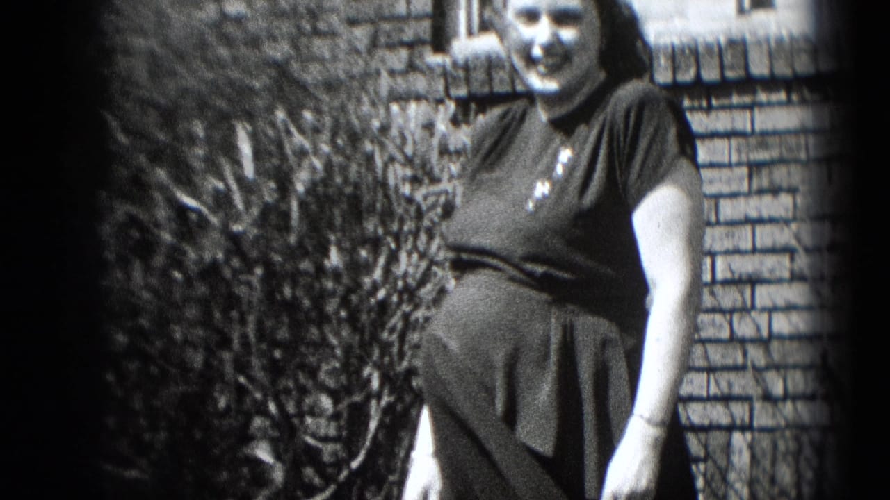 In Middletown, Pennsylvania home-movie footage, a pregnant woman in a dark dress smiles outdoors near a brick wall and shrubs.