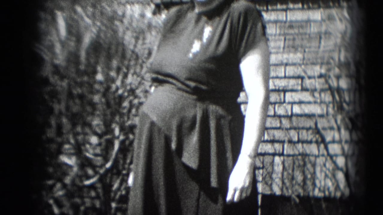 Pregnant woman in a dark dress poses outside a brick house in metadata-identified Middletown, Pennsylvania archival home-movie footage.
