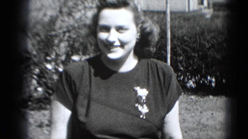The woman smiles warmly toward the camera in this 1948 Middletown home-movie frame, standing near shrubs and lawn.