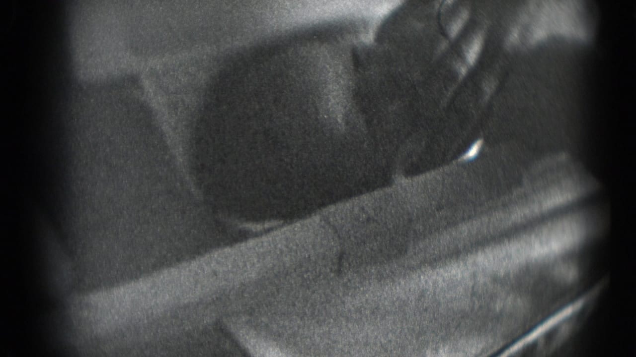 Grainy black-and-white 8mm frame showing a newborn's head on bedding or cloth with a hand near the face.