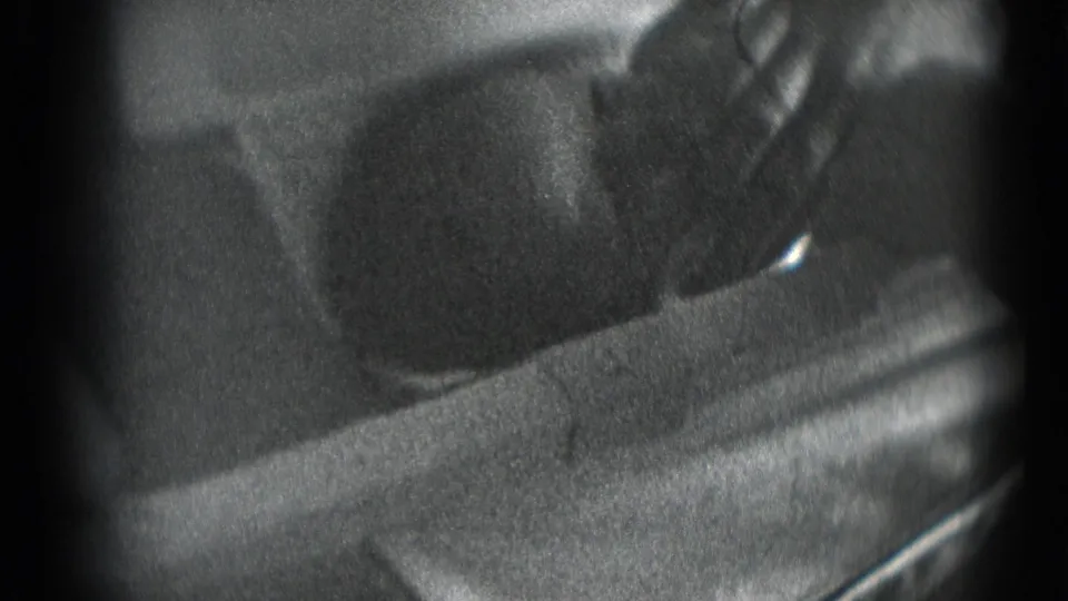 Grainy black-and-white 8mm frame showing a newborn's head on bedding or cloth with a hand near the face.