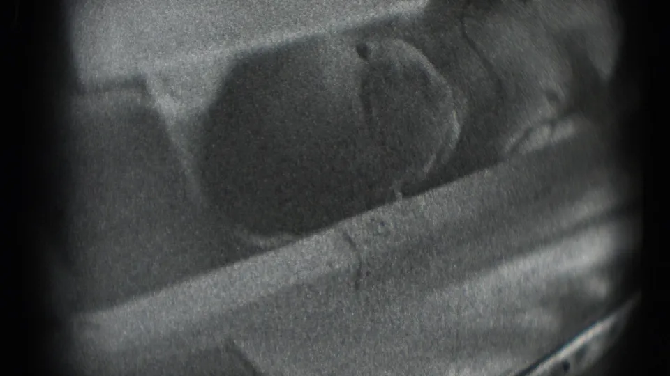 Soft black-and-white 8mm close-up of a newborn resting on cloth, with the face partly turned and blurred by motion or focus.