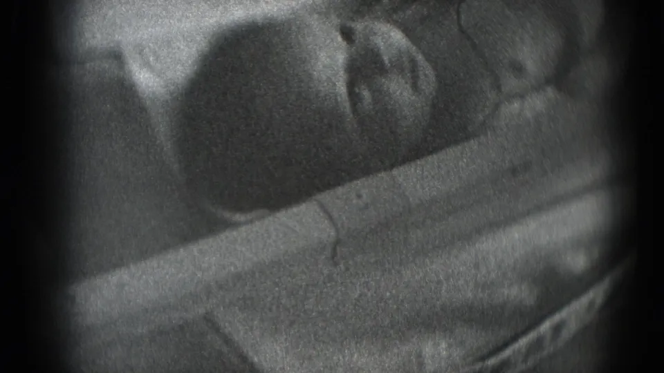 Black-and-white 8mm close-up of a newborn's face and head resting on cloth, framed by dark film edges.