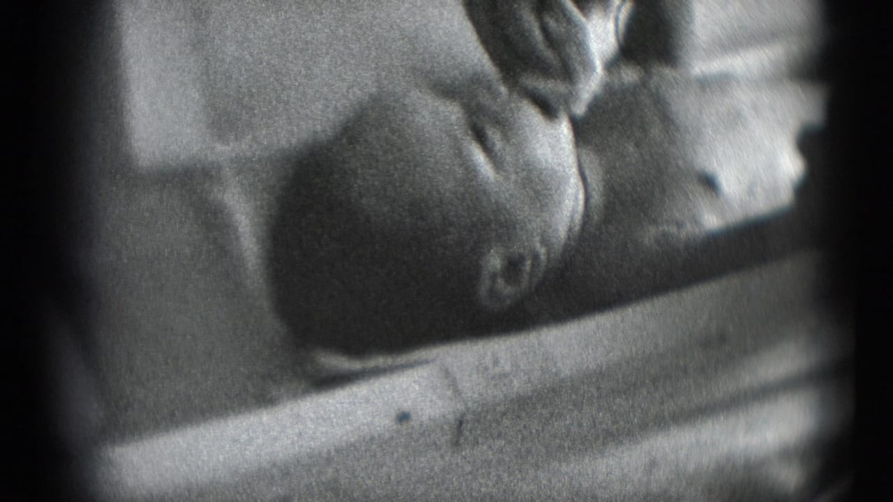 1940s 8mm home-movie frame from Middletown, Pennsylvania, showing an adult hand tending to a baby lying on its back.