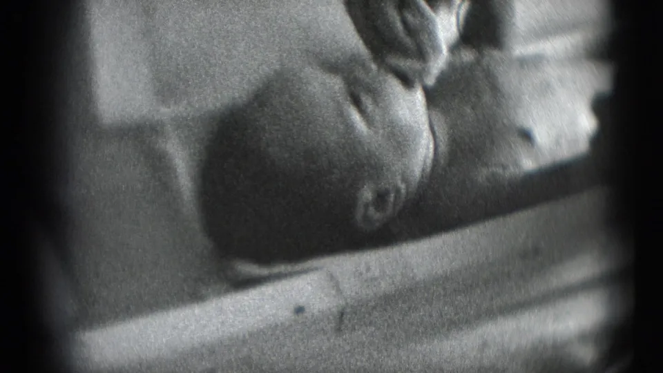 1940s 8mm home-movie frame from Middletown, Pennsylvania, showing an adult hand tending to a baby lying on its back.