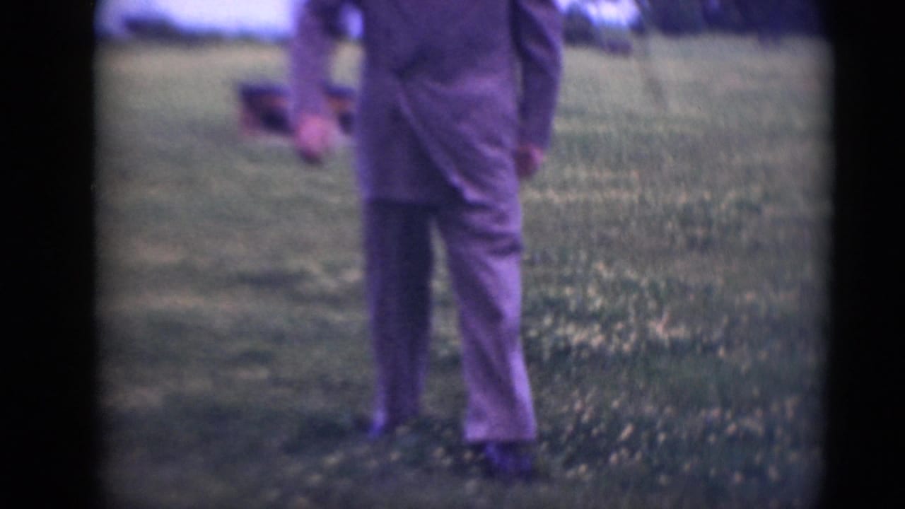 Adult man in a gray suit partly framed in a grassy field.
