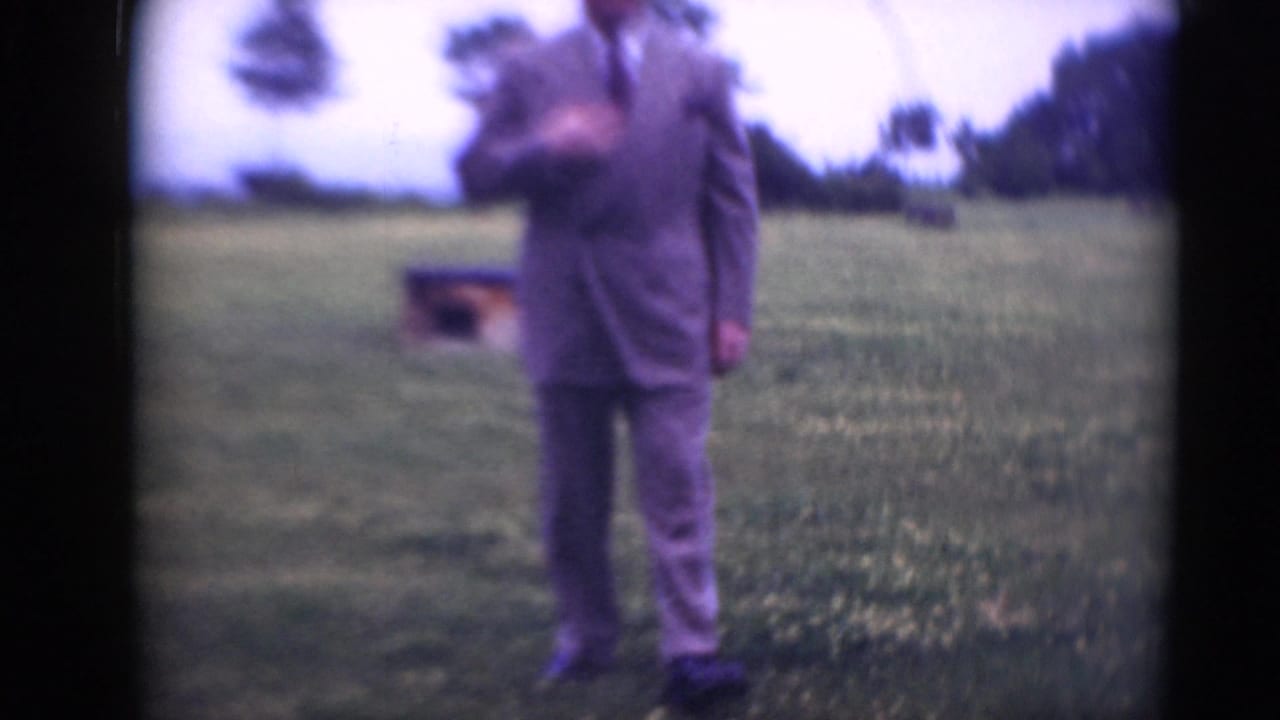 Adult man in a gray suit stands outdoors in a grassy Middletown, Pennsylvania field, with trees and a small low structure behind him.
