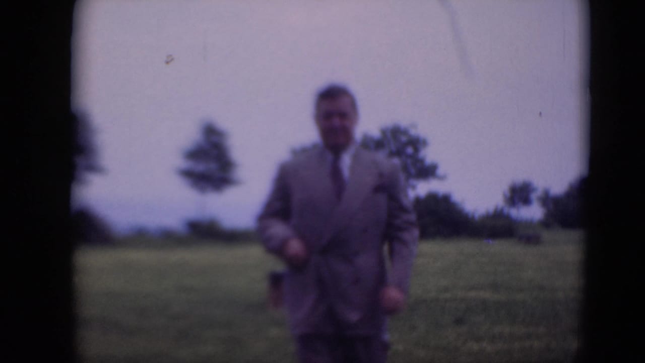 The man in formal clothing walks nearer to the camera in the 1948 Middletown field scene, with soft focus and visible film borders.