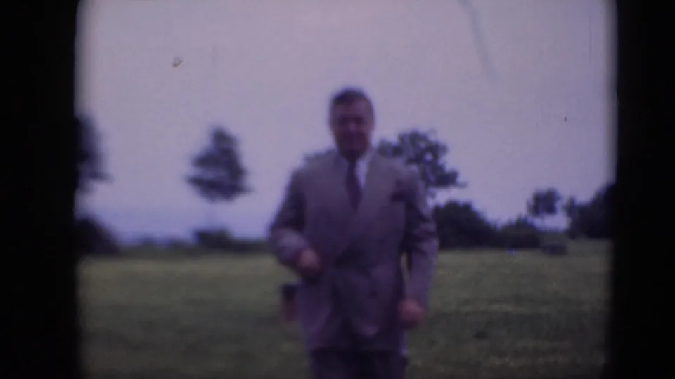 The man in formal clothing walks nearer to the camera in the 1948 Middletown field scene, with soft focus and visible film borders.