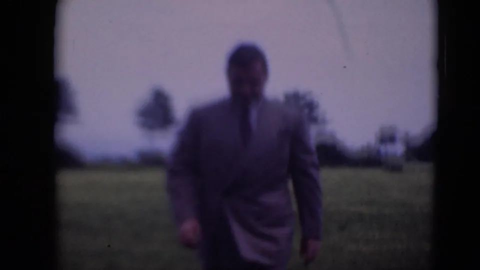 A closer, softly focused view shows the suited man continuing toward camera in the Middletown home-movie field shot.
