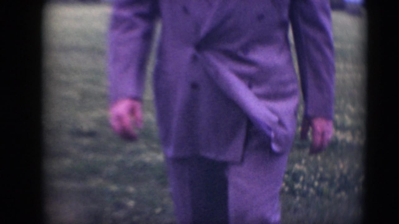 Man in a light suit walks across grass, cropped from neck to knees.