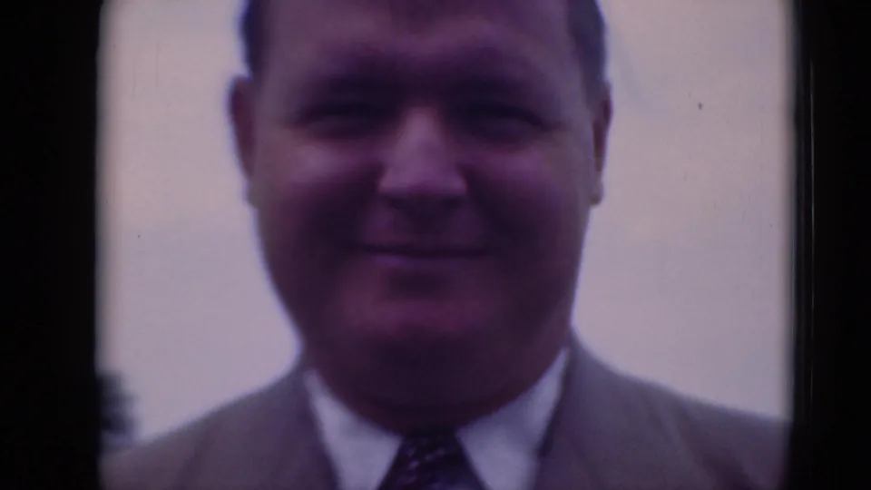 A softly focused close-up shows the suited man smiling toward the home-movie camera.